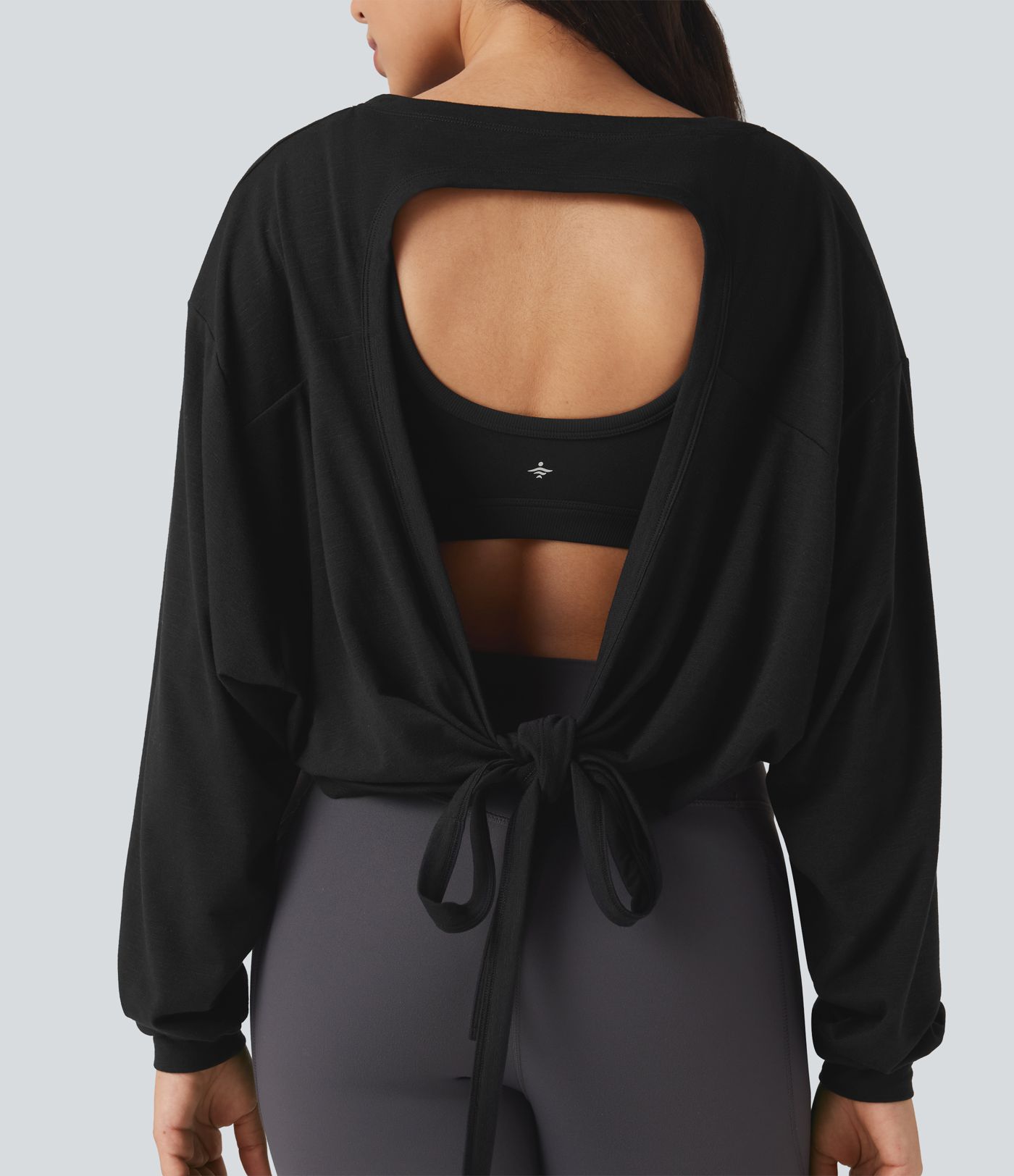 Top deportivo para correr de cuello redondo, manga larga, con aberturas y lazo en la espalda.