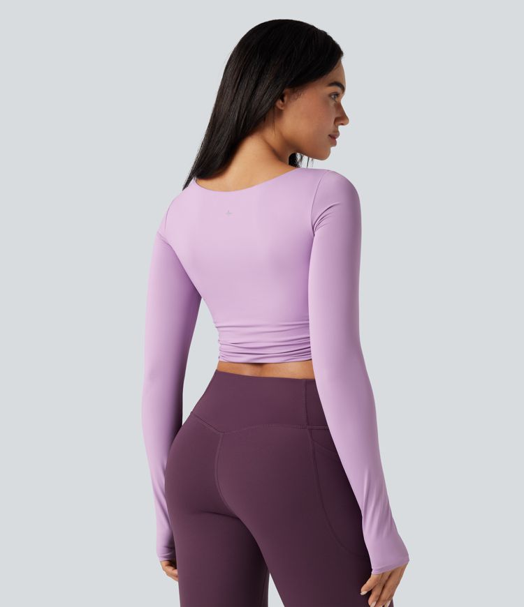 Trumpintas jogos sportinis topas su push-up efektu, formuotais spacer kaušeliais, apvalia iškirpte, ilgomis rankovėmis su nykščių angomis ir kryžminiu dizainu.